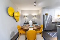 Chic dining area with vibrant yellow chairs and modern decor, next to a sleek stainless steel kitchen in a stylish apartment.