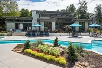 Luxurious apartment complex with a modern poolside, elegant outdoor seating, and vibrant landscaping under a clear sky.