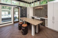 Modern and elegant kitchen with sleek countertops, unique barrel-style stools, wine storage, and large windows offering a bright and airy feel.