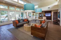 Inviting modern living room with large windows, stylish wood furniture, colorful cushions, and chic lighting, overlooking a serene outdoor pool area.