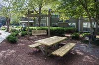 Charming outdoor area featuring a wooden picnic table and a cozy swing bench under the shade of lush green trees, perfect for relaxation and gatherings.