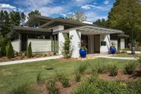 Modern home with sleek architecture, lush landscaping, and vibrant blue planters, set against a clear sky and surrounded by greenery.