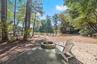 Serene lakeside view with cozy Adirondack chairs, surrounded by lush trees and a picturesque firepit, perfect for relaxation and nature appreciation.