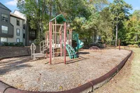 Inviting playground nestled in a serene apartment community, featuring a vibrant play structure surrounded by lush trees and well-maintained grounds.