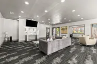 Elegant communal living area with a modern gray sofa, stylish accent chairs, and a large flat-screen TV, accented by contemporary decor and ample lighting.