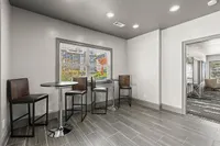 Elegant modern seating area with high stools and tables, featuring large windows and sleek gray tile flooring, perfect for casual gatherings.
