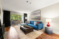 Elegant living room with a stylish blue sofa, modern artwork, and floor-to-ceiling windows opening to a lush balcony view. Perfect blend of comfort and style.