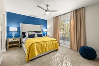 Bright, elegant bedroom featuring a plush bed with vibrant yellow bedding, blue accent wall, and large sunlit window, perfect for a cozy and inviting atmosphere.