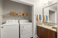 Chic laundry and bathroom area featuring modern washer and dryer, sleek granite countertop, and stylish wicker storage baskets.