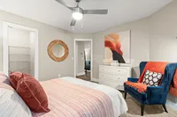 Inviting bedroom with modern decor, featuring a cozy bed with colorful pillows, a stylish blue armchair, and elegant artwork on the wall.