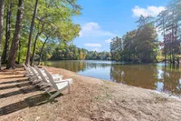 Tranquil lakeside scene featuring white Adirondack chairs under tall trees, perfect for relaxing and enjoying nature's beauty.