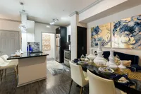 Elegant modern kitchen and dining area featuring sleek black cabinetry, stainless steel appliances, and chic pendant lighting. The stylish dining table is adorned with decorative white vases and vibrant artwork accents the walls, adding sophistication to the space.