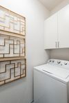 Modern laundry room with sleek white cabinetry and decorative golden wall art.