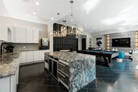 Luxurious apartment interior showcasing a sleek modern kitchen with elegant marble countertops, chic lighting, and an inviting entertainment area with a billiards table and stylish lounge seating.