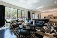 Luxurious open-concept living room with modern decor, featuring large windows, stylish seating, and a sleek kitchen space.