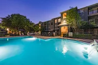 Luxurious apartment complex at dusk featuring a shimmering swimming pool surrounded by lush greenery and inviting lounge chairs.