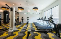 Modern gym with sleek treadmills, rowing machine, and punching bag on vibrant geometric flooring, illuminated by stylish overhead lights.