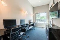 Modern apartment business center with sleek workstations, stylish chairs, and natural light from large window creating an inspiring workspace.