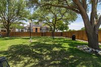 Inviting apartment community outdoor area with lush green lawn, mature trees, and charming wooden fence under a clear blue sky.
