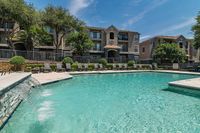 Charming apartment complex with lush landscaping, featuring a stunning outdoor pool and relaxing lounge chairs under the bright blue sky.