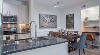 Modern kitchen and dining area with sleek granite countertops, elegant backsplash, and ambient lighting, complemented by artistic wall decor and a cozy desk nook.