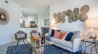 Bright and modern living room with elegant decor, featuring colorful cushions, unique wall art, and a cozy seating area leading to an open kitchen.