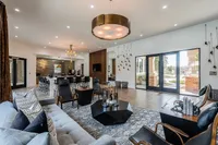 Spacious and elegant living area with modern decor, featuring a plush gray sofa, stylish seating, chic lighting, and floor-to-ceiling windows opening to a serene garden view.