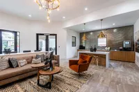 Elegant open-concept living space featuring a plush sofa, modern lighting, and a stylish kitchen with brick backsplash and gold accents.
