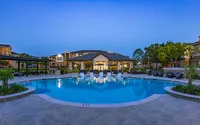Luxurious apartment complex featuring a sparkling pool, elegant loungers, and serene landscaping at dusk.