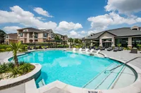 Luxurious apartment complex with a stunning outdoor pool, surrounded by lush greenery and stylish lounge chairs, perfect for relaxation and leisure.