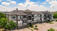 Elegant apartment complex with modern architecture and lush greenery under a bright blue sky.