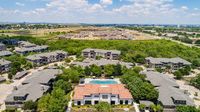 Aerial view of a lush apartment community with modern buildings, centered around a sparkling pool and surrounded by green spaces, offering tranquil suburban living.
