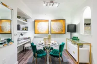 Chic dining area with elegant decor, featuring a glass table with green velvet chairs and modern art pieces on the wall.