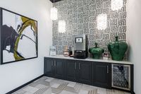 Chic coffee station with modern art and geometric wallpaper, featuring a sleek countertop, coffee machine, vibrant green vases, and wine cooler.