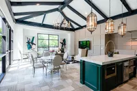 Elegant living space with vaulted beamed ceilings, modern chandeliers, and a stylish open concept kitchen-dining area.