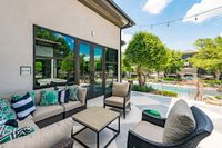 Charming outdoor patio with elegant wicker seating and vibrant cushions, overlooking a serene swimming pool surrounded by lush greenery.
