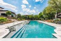Luxurious outdoor pool area with modern lounge chairs, surrounded by lush greenery and vibrant floral landscaping under a bright blue sky.