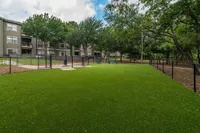 Serene apartment community with lush green lawn, cozy benches, and shaded pathways surrounded by mature trees.
