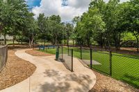 Scenic outdoor space featuring lush greenery, walking paths, and a fenced area perfect for relaxation and play.