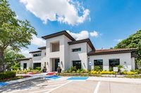 Elegant residential building surrounded by lush landscaping and clear blue skies, showcasing modern architecture with clean lines and large windows.