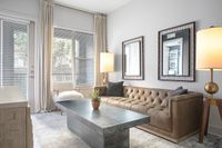 Elegant living room with a plush tufted leather sofa, modern coffee table, and floor-to-ceiling windows allowing natural light to flood the room.