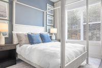 Elegant bedroom with a cozy white canopy bed, plush pillows, and soft lighting, featuring large windows for natural light.