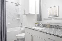 Elegant bathroom featuring a modern granite countertop, white cabinetry, and a luxurious tiled bathtub with a rainfall showerhead.