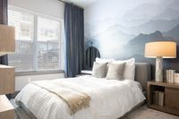 Serene bedroom with soft lighting, featuring a cozy bed, elegant side table, and artistic mountain-themed wall design.