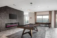 Contemporary game room with modern pool table, sleek fireplace, and large windows for natural light.