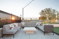 Chic rooftop patio with modern gray seating, a stylish table, and stunning cityscape views at sunset.