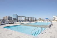 Luxury rooftop pool with chic lounge chairs, modern cabanas, and stunning city skyline views under a clear blue sky.