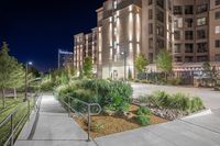 Elegant nighttime view of a modern apartment complex with beautifully landscaped paths, highlighted by strategic lighting.