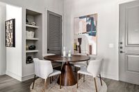 Elegantly designed dining nook featuring a round wooden table, four modern chairs, and contemporary artwork on light-toned walls.