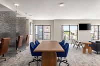 Modern communal workspace featuring elegant wooden table, stylish blue and brown chairs, and expansive windows letting in natural light.
